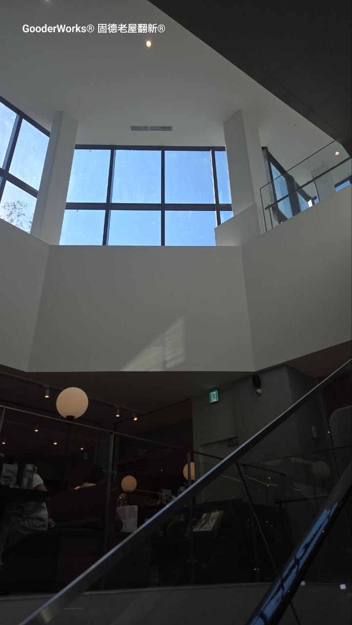 建築物內部樓梯間採光實景:大面積落地窗引入自然光,白色幾何牆面與玻璃欄杆展現現代簡約風格