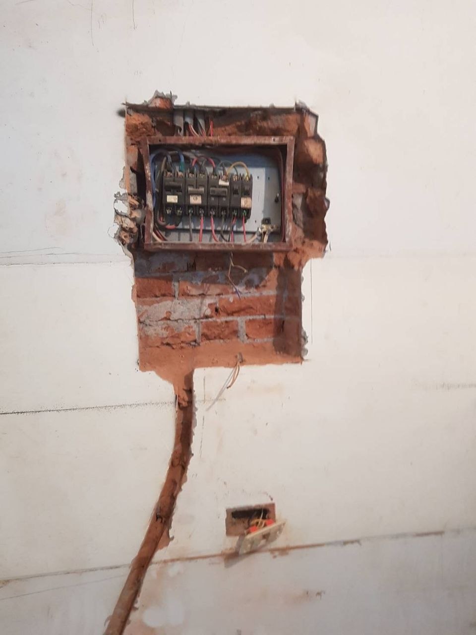 老屋電箱危險現場:牆壁挖開裸出紅磚,電箱嵌在牆上內部黑色無熔線開關老舊,電線混亂糾結,下方開關盒半開