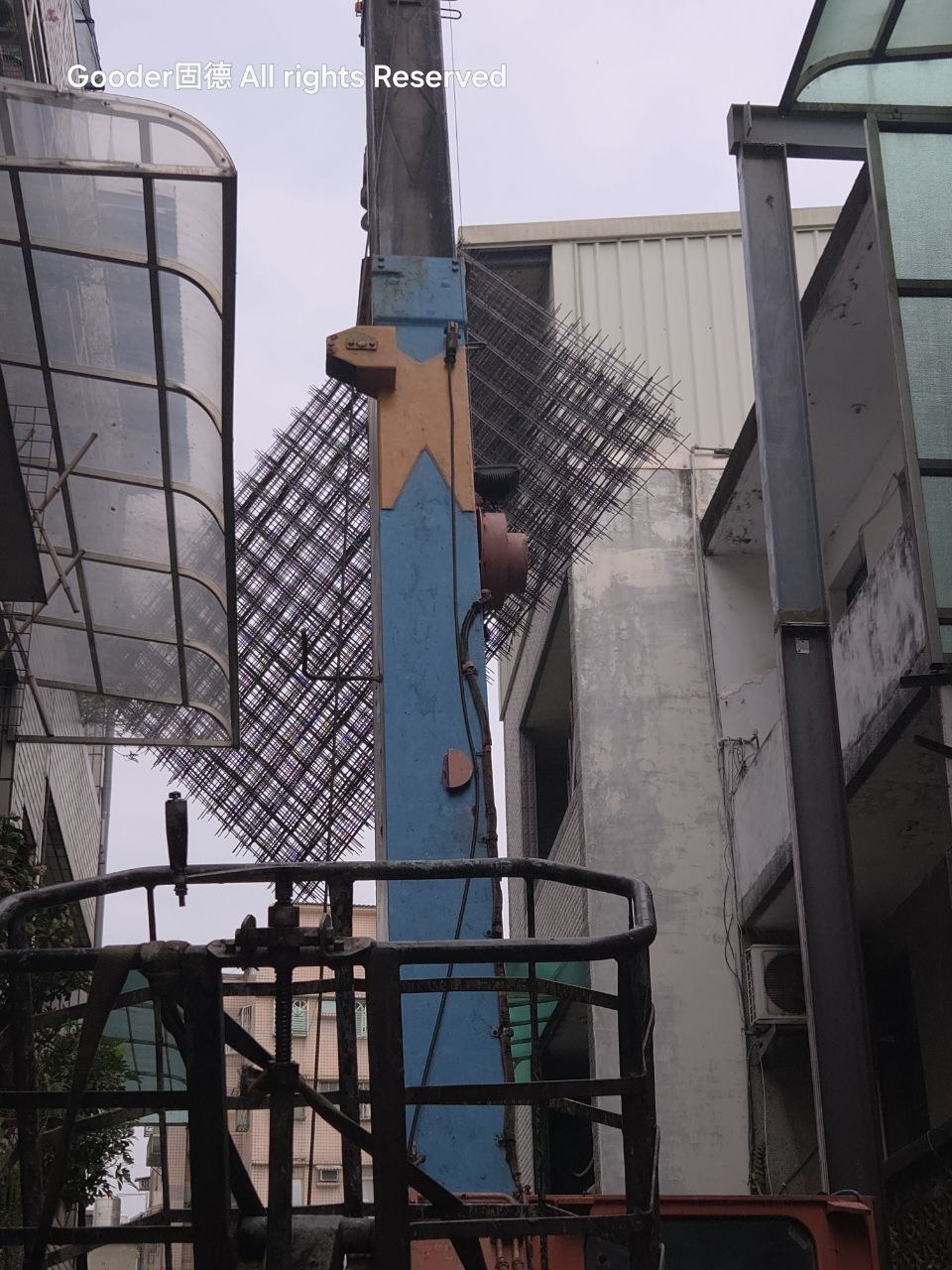 工地吊車吊運大型點焊鋼絲網片,準備送往施工現場,前景是黑色金屬吊籃